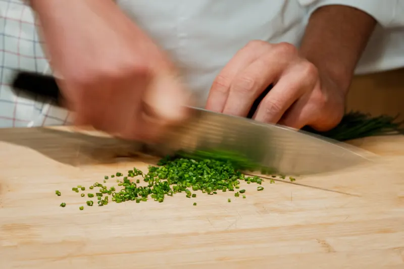 Ciboulette finement ciselée au couteau sur une planche en bois
