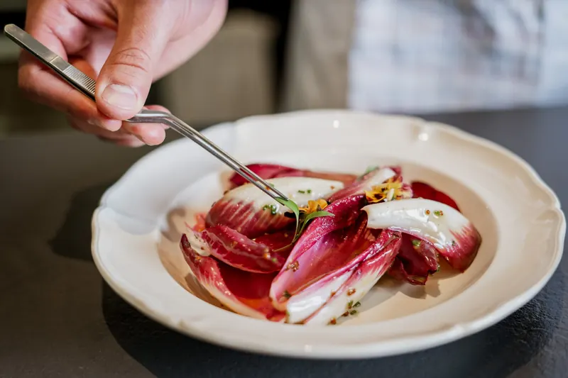 Finition à la pince d’une salade d’endives rouges décorée de pensées