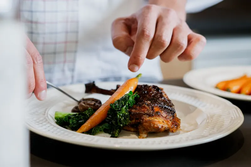 Dernières retouches sur une assiette de volaille, carotte et chou kale