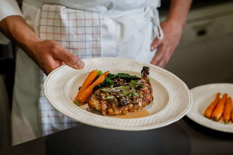 Le chef tient une assiette de volaille, carottes glacées et chou kale